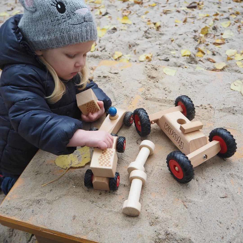 Mädchen spielt im Herbst mit rewoodo Holzspielzeug Kibbly und RibbleRace im Sandkasten