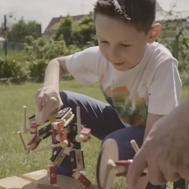 Kleiner Junge spielt mit den Helden aus Holz und seinem Vater im Sommer im Garten - Outdoor Holzspielzeug